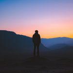 silhouette of man standing on mountain during sunset